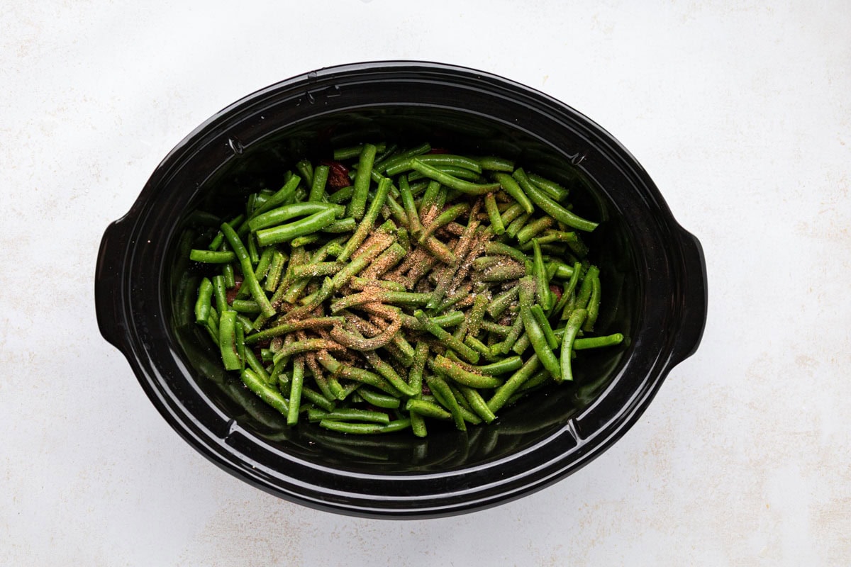 Green beans and seasonings added to the potatoes in a crockpot.