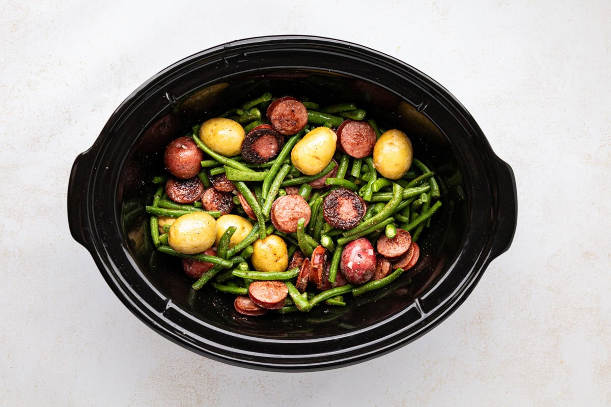Sausage, potatoes and green beans mixed together in a slow cooker.