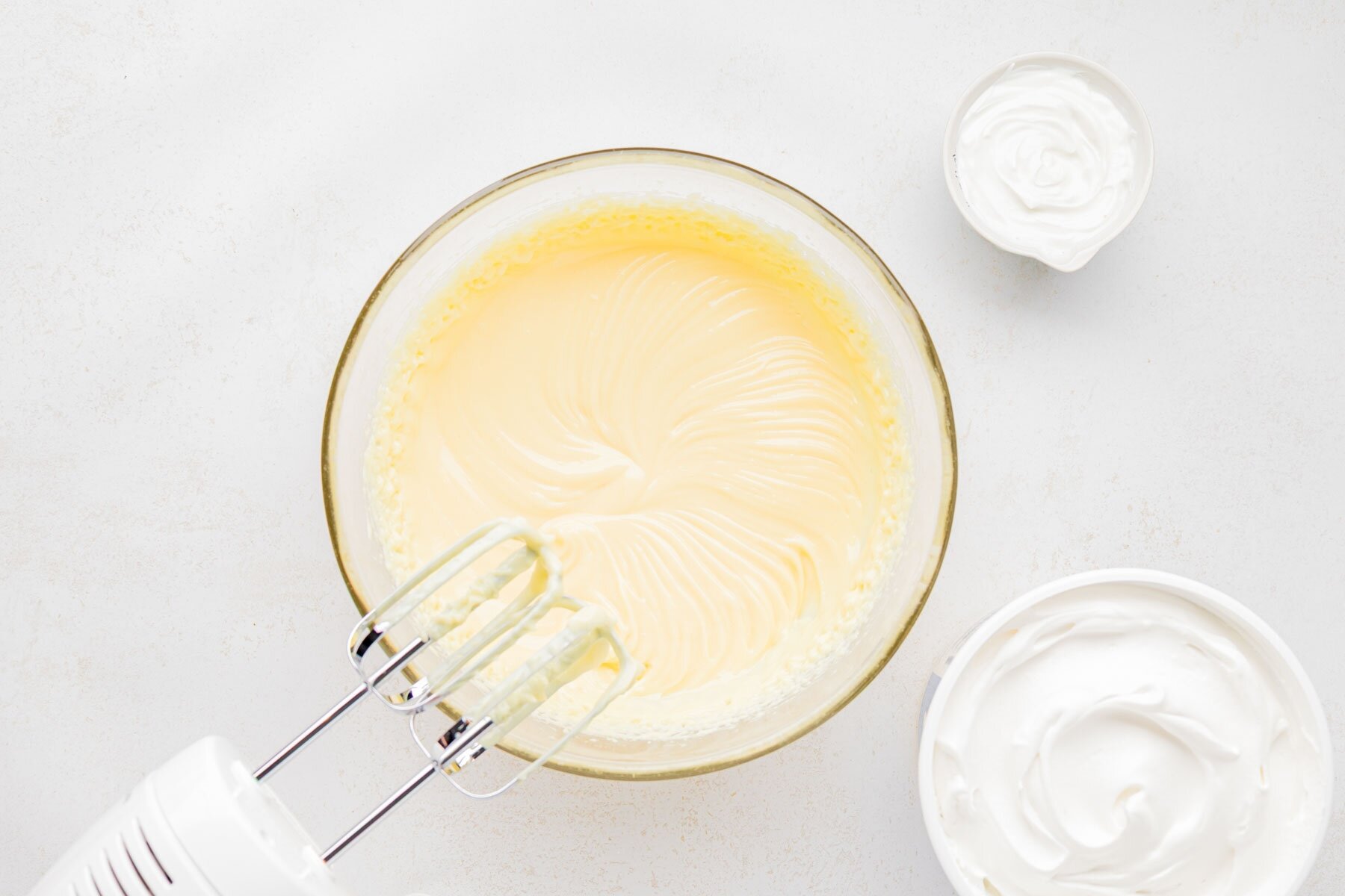 Electric beaters mixing pudding mixture in a large glass bowl.