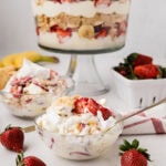 A serving of strawberry banana pudding with the trifle dish in the background.