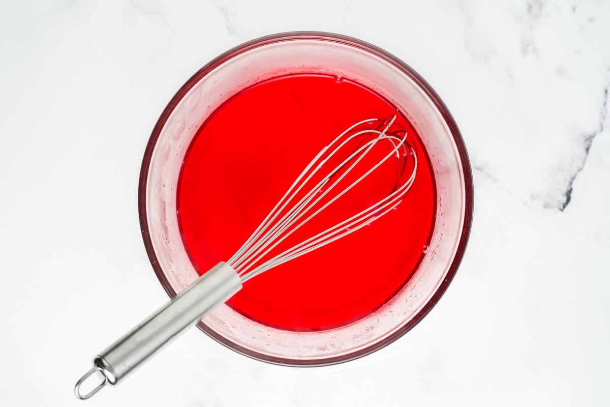 Mixing strawberry jello and water in a bowl.