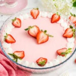 Strawberry jello pie in a glass pie dish with whipped cream and fresh strawberries on top.