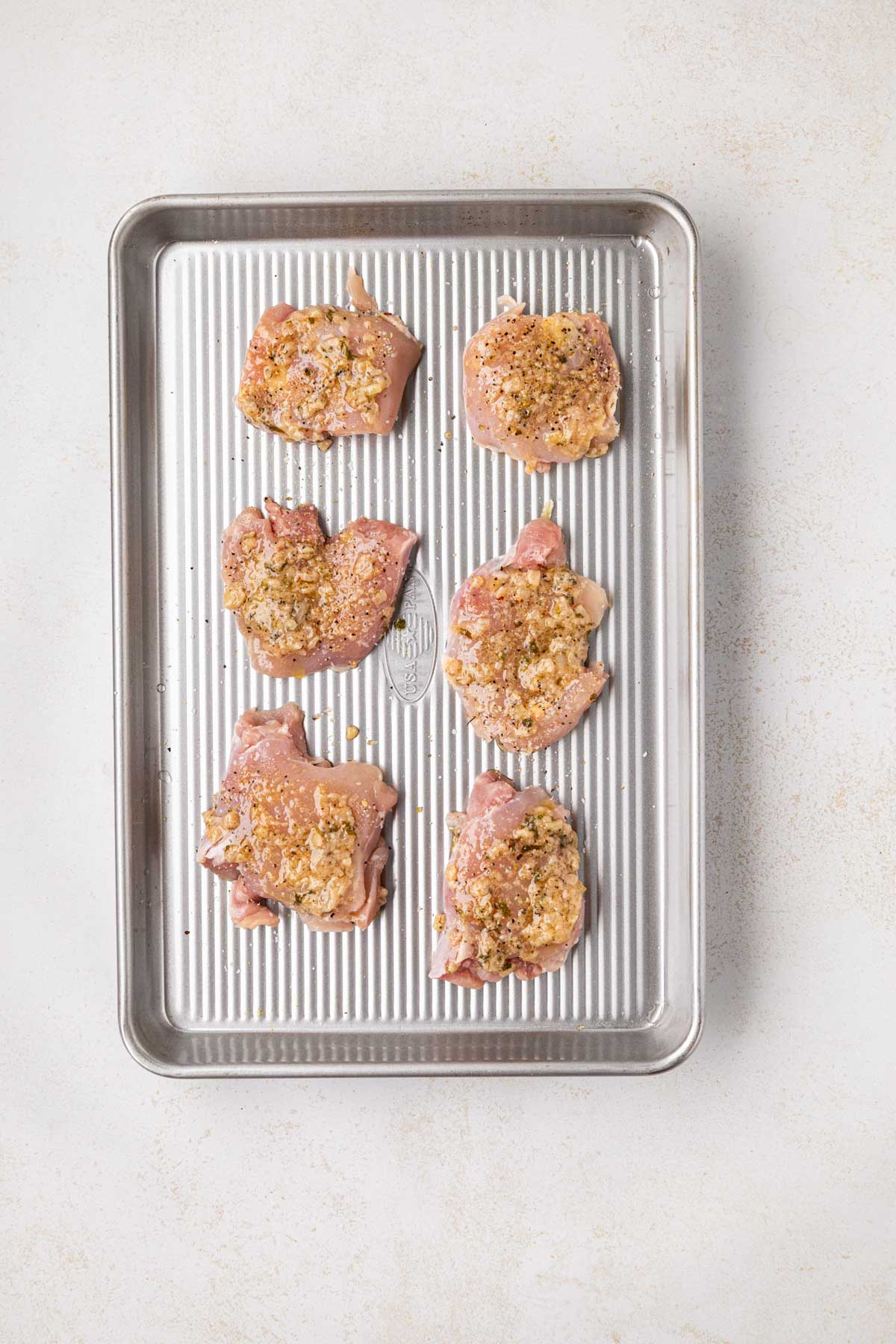 Chicken thighs on a sheet pan with seasoning and Italian grill baste.