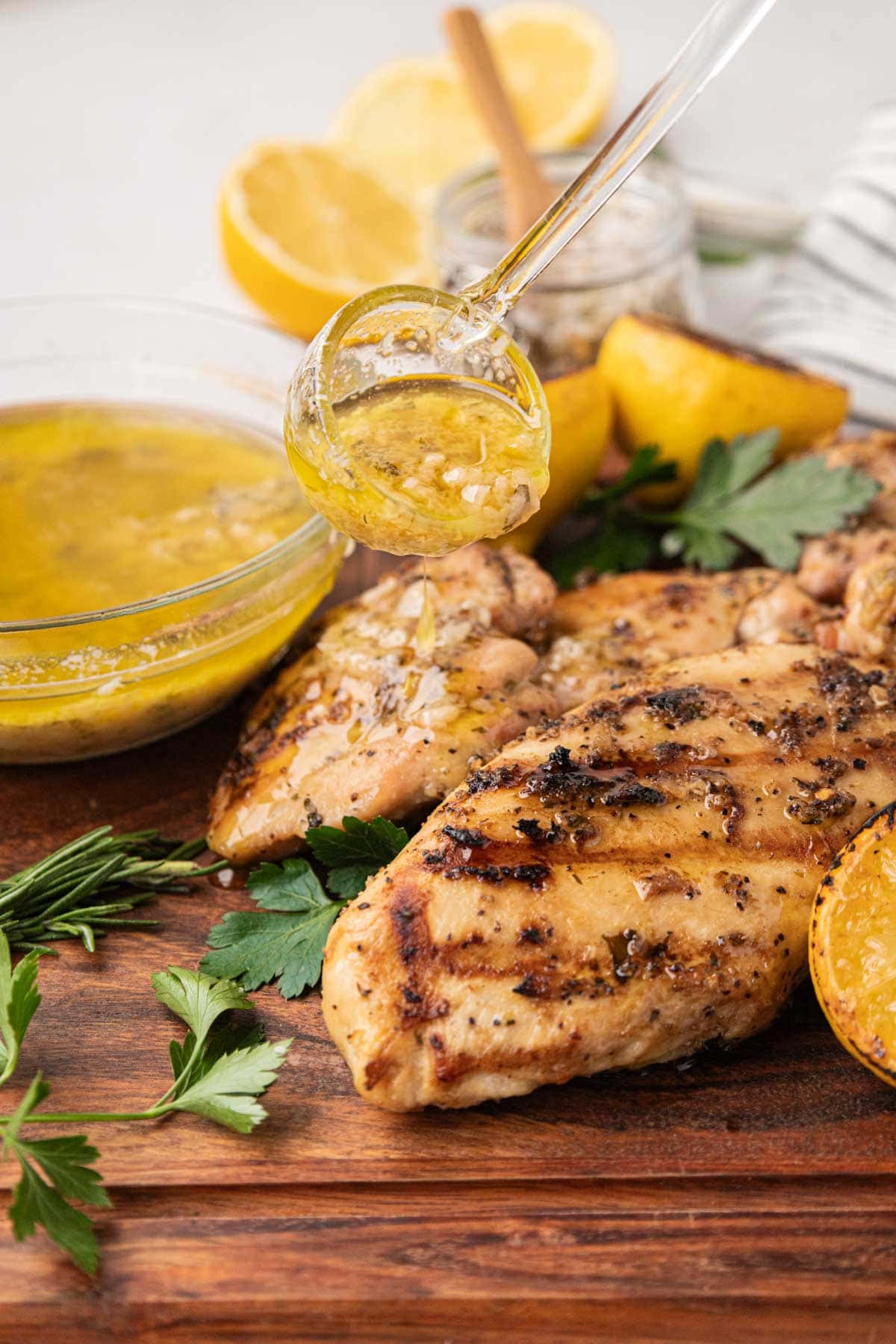 Butter herb mixture being poured over tuscan Italian grilled chicken on a wooden board.