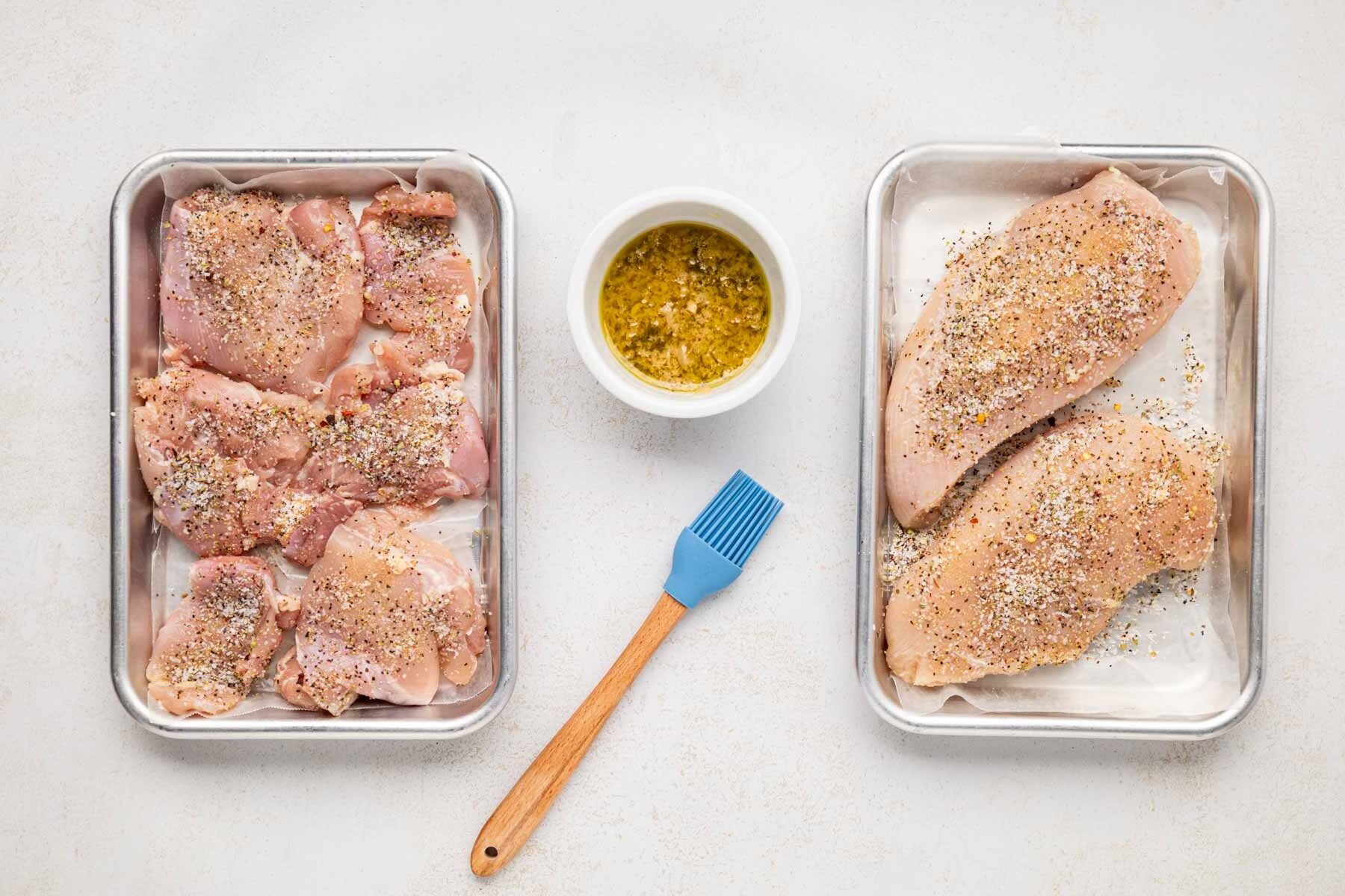 Chicken breasts and thighs on baking sheets sprinkled with Italian grill seasoning.