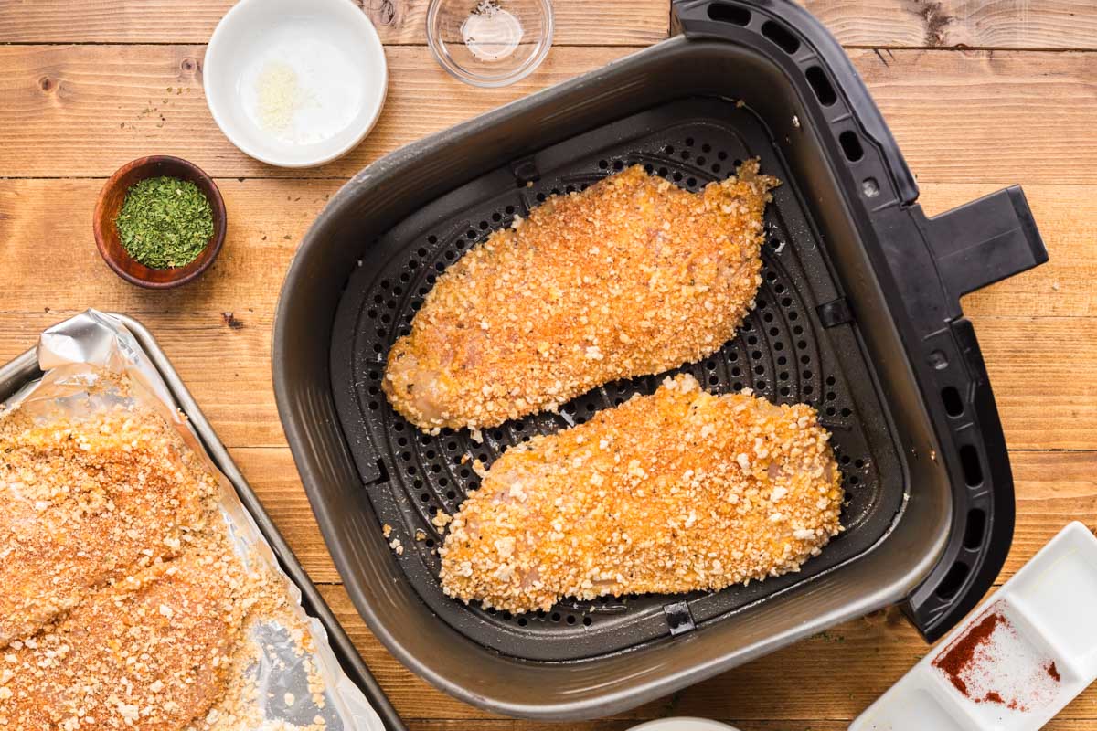 Breaded chicken cutlets in the air fryer basket to cook.