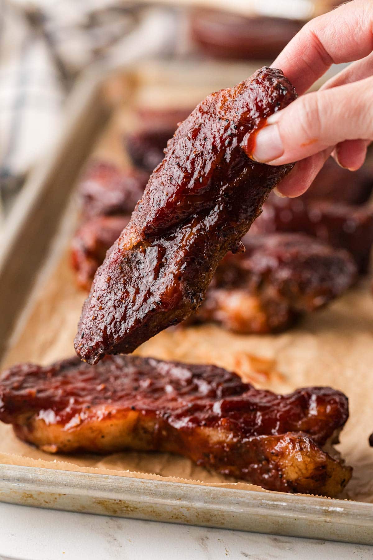A hand picking up a rib from the pan.