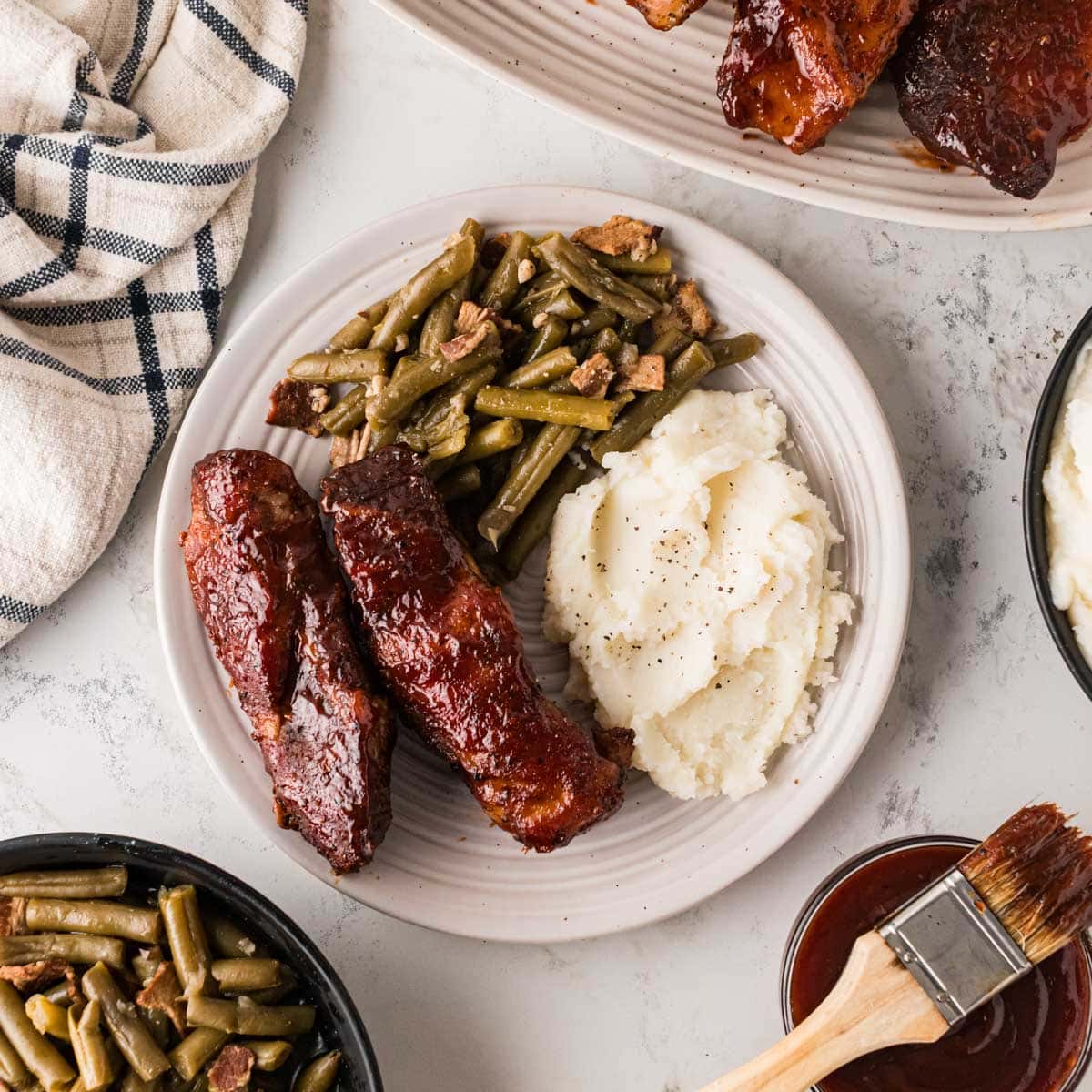 Two country style bbq ribs on a white plate with mashed potatoes and green beans.