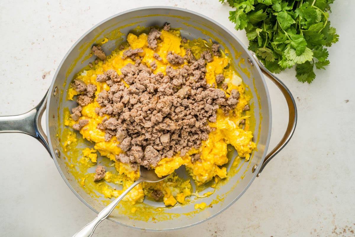 Combining scrambled eggs with sausage in a skillet.