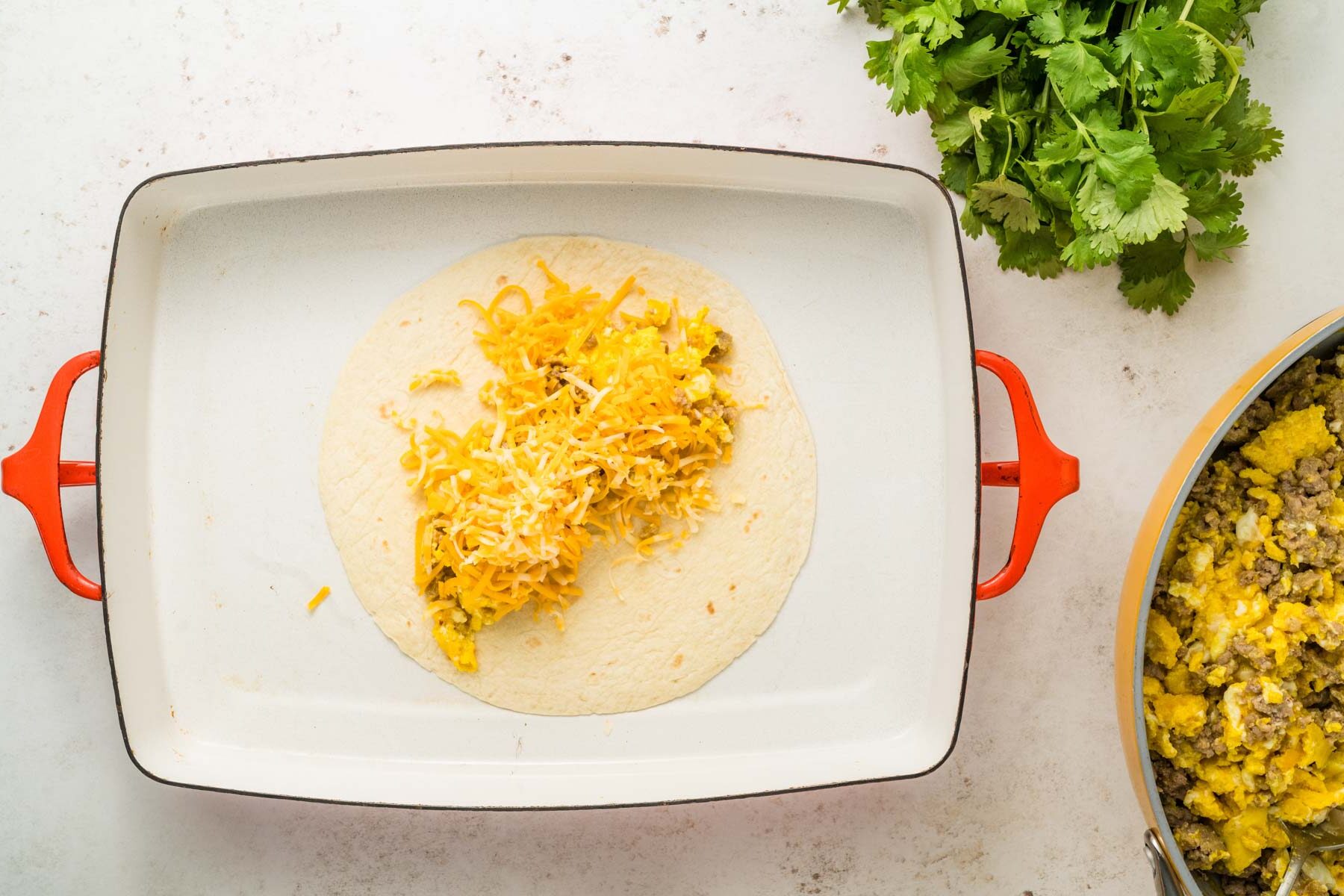 Adding cheese to the breakfast enchilada in a baking dish.