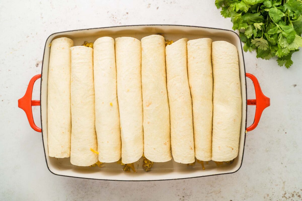 All rolled and assembled enchiladas in a baking dish.
