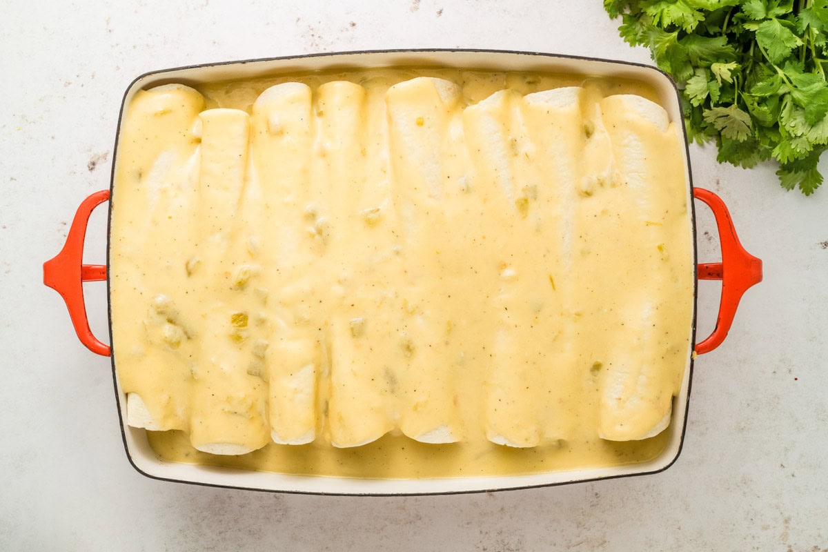 Cheese sauce poured over the top of the assembled breakfast enchiladas before baking.