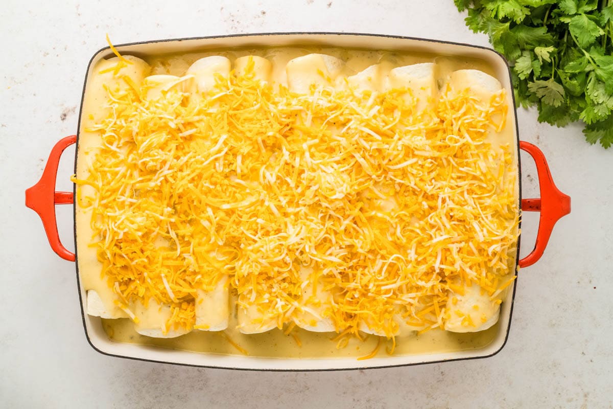 Shedded cheese sprinkled on top of the cheese sauce on the breakfast enchiladas.