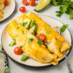 Two breakfast enchiladas on a plate garnished with cilantro diced avocado, and tomatoes.