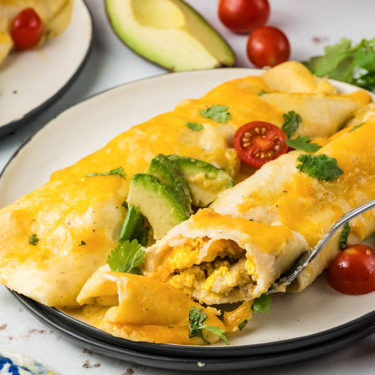 Close up of two breakfast enchiladas on a plate with a fork taking a bite.