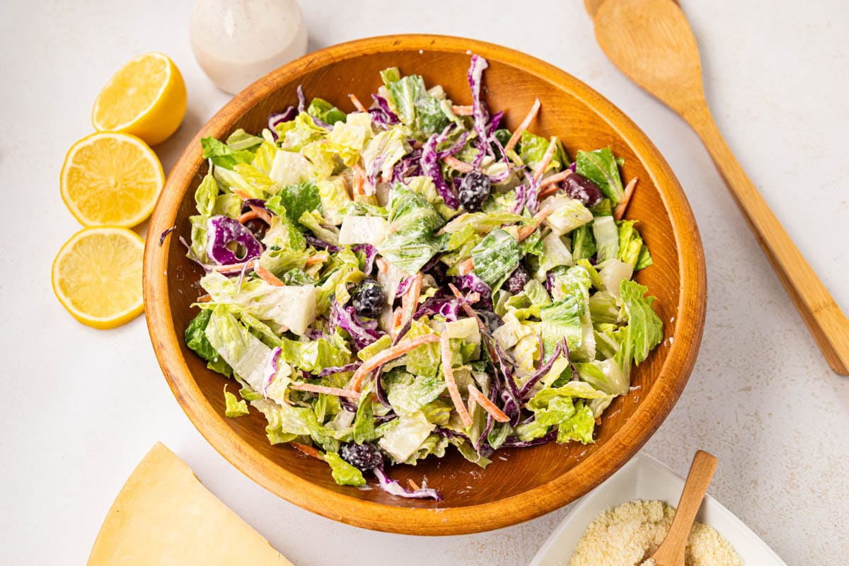 Creamy Parmesan house salad with the dressing tossed to coat the salad in a wooden bowl.
