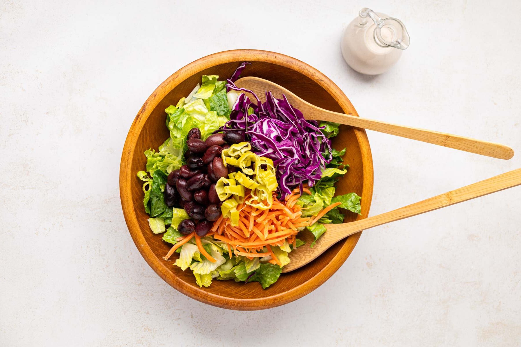Lettuce, red cabbage, carrots, pepperoncini peppers and kalamata olives added to a wooden salad bowl.