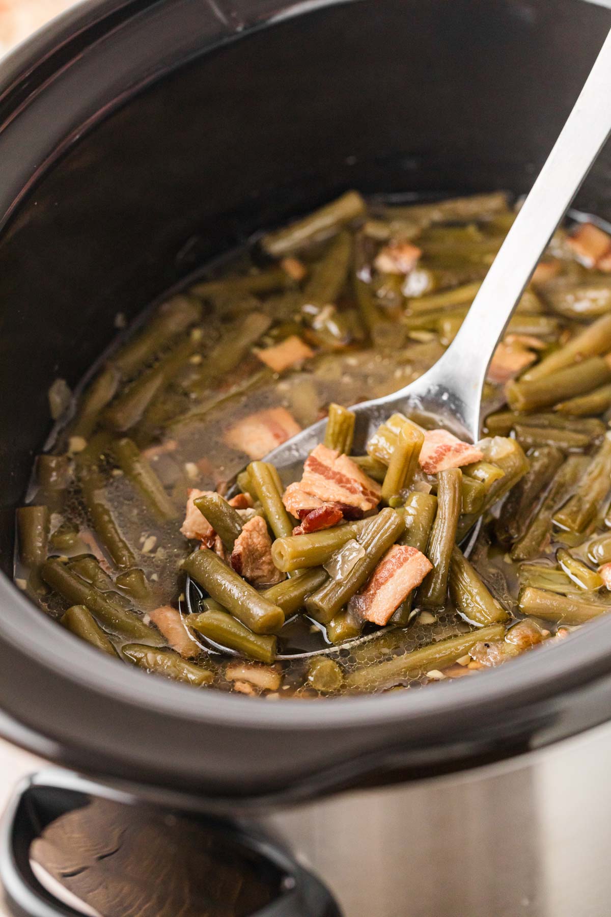 A serving spoon scooping out a serving of green beans from the slow cooker.