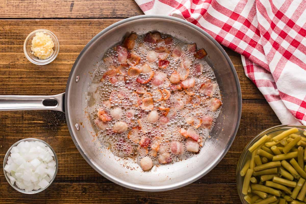 A skillet frying pieces of bacon.