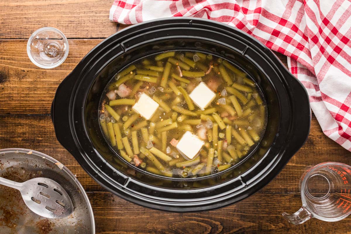 Pats of butter added on top of the green beans in the slow cooker.