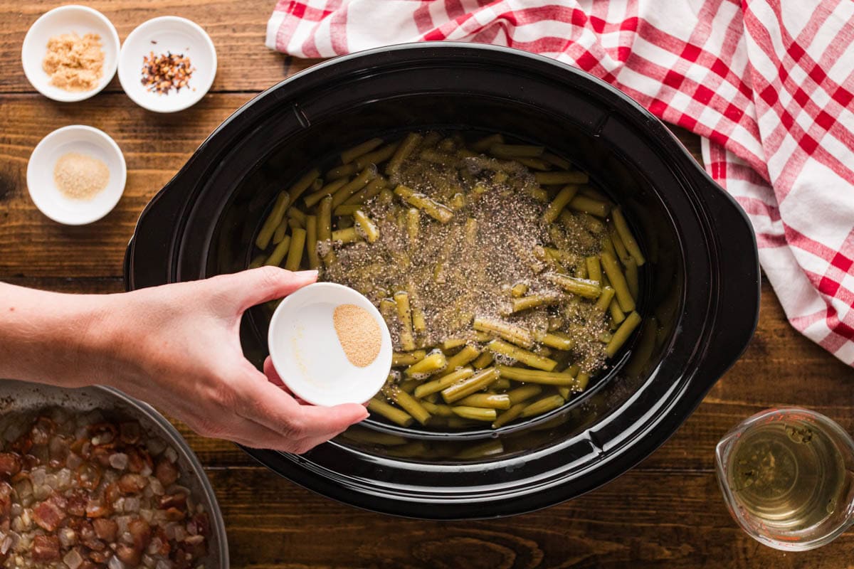 Pouring seasonings into the crock pot with the green beans.