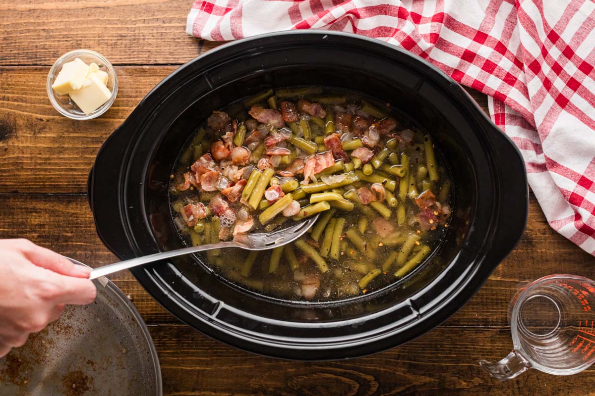 A slotted spoon being used to add the bacon mixture into the crock pot.
