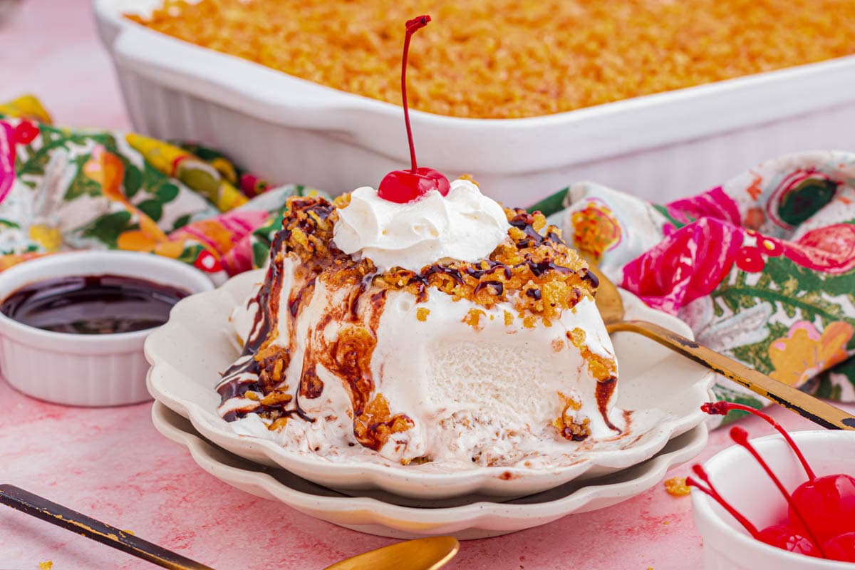 A slice of fried ice cream cake drizzle with chocolate and topped with whipped cream and a cherry with a bite taken out.