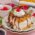 A slice of fried ice cream cake drizzle with chocolate and topped with whipped cream and a cherry.