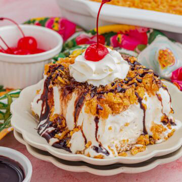 A slice of fried ice cream cake drizzle with chocolate and topped with whipped cream and a cherry.
