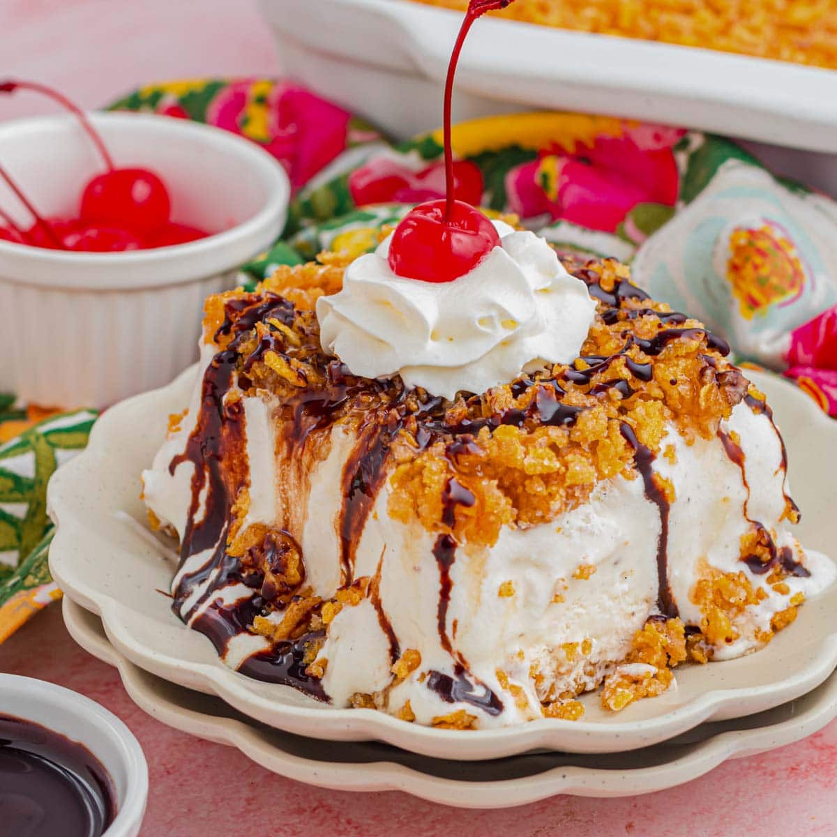 A slice of fried ice cream cake drizzle with chocolate and topped with whipped cream and a cherry.