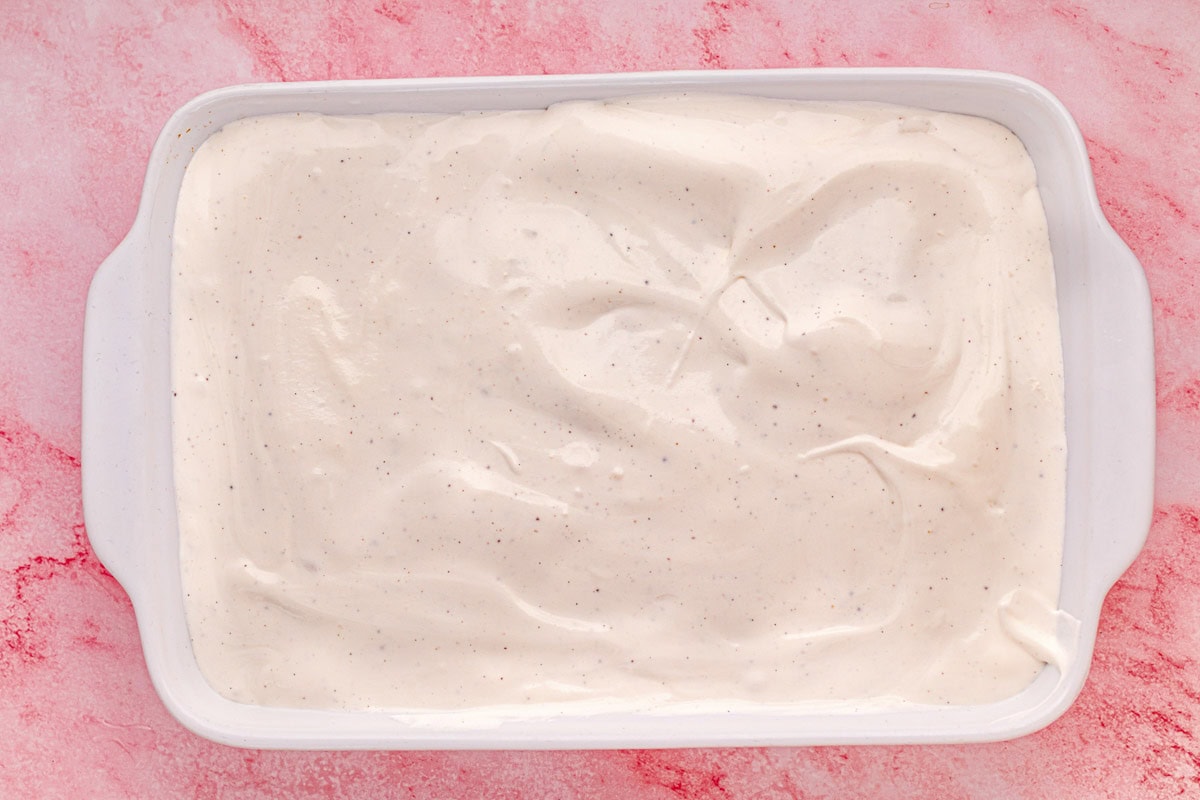 Ice cream layer added on top of crust in a baking dish.