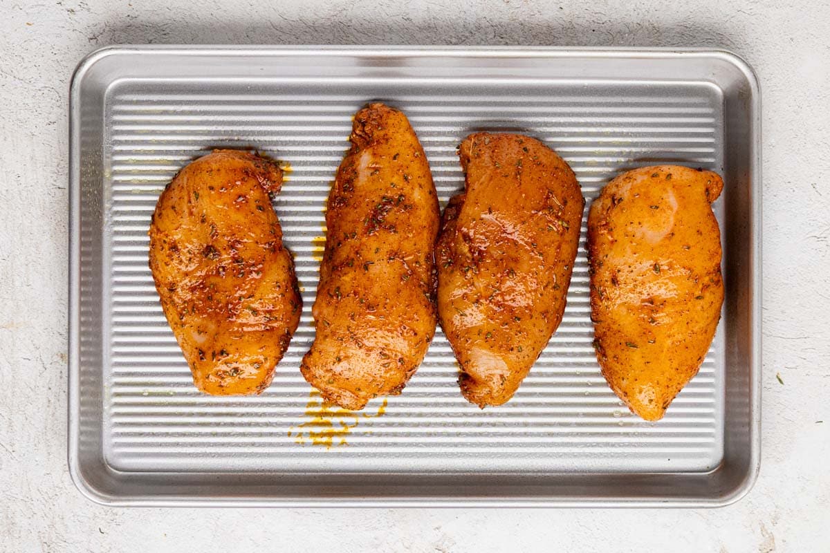 Uncooked seasoning chicken on a baking sheet.