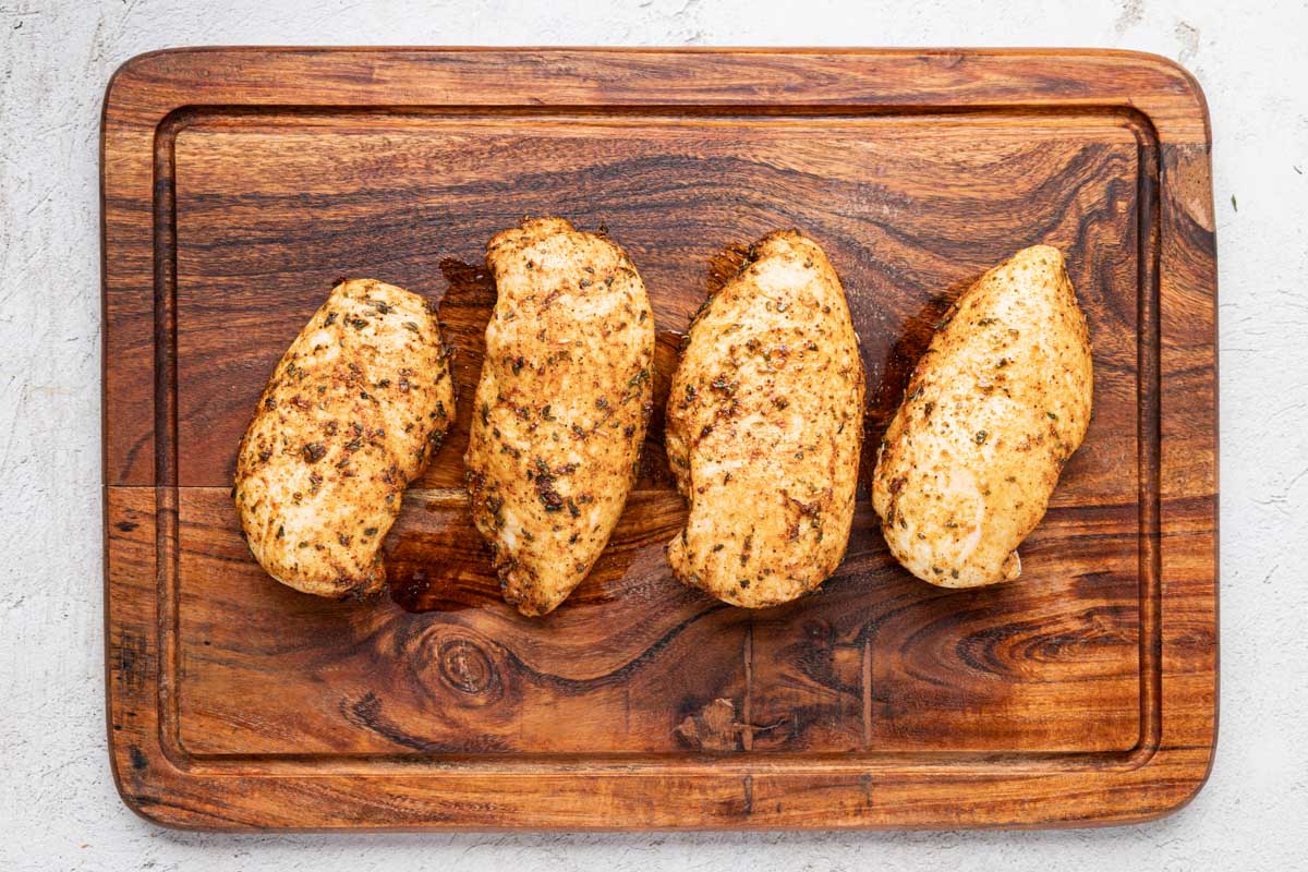 Cooked baked chicken on a wooden cutting board to rest.