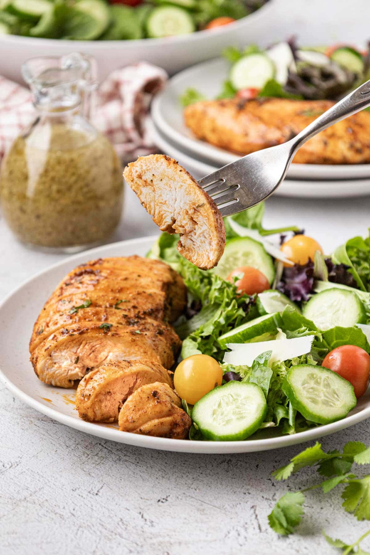 A fork, removing a bite of juicy chicken breast from a plate with a side salad.