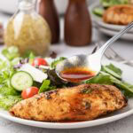 Pan juices spooned over oven baked chicken on a plate.