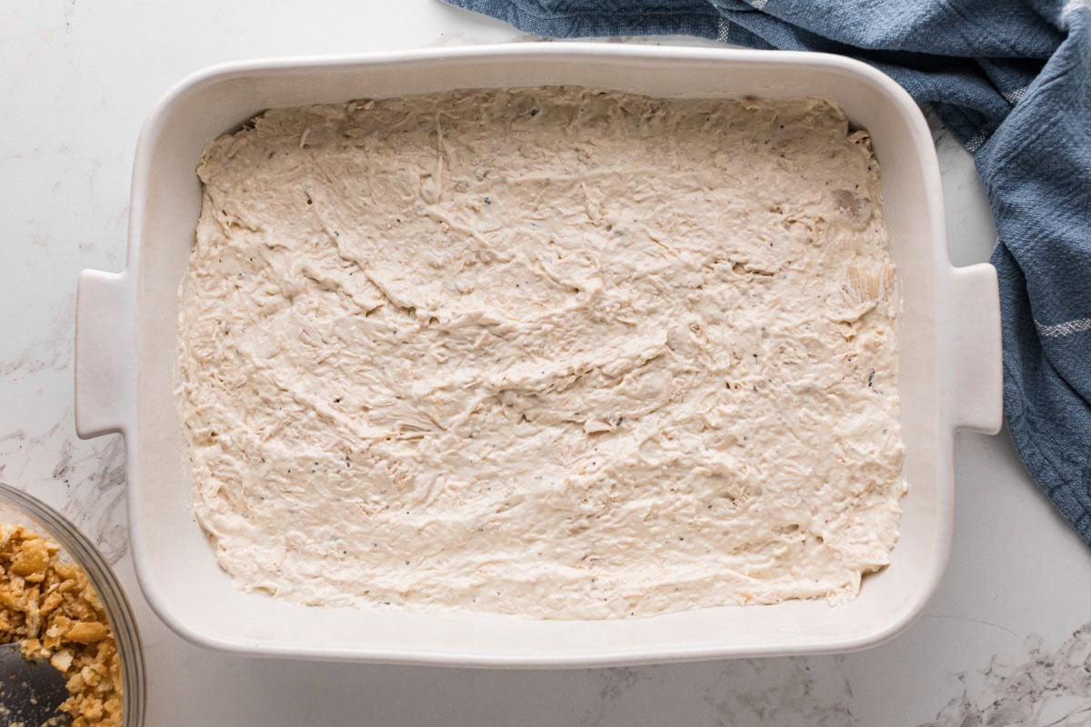 Layer of chicken casserole mixture in the bottom of a white baking dish.