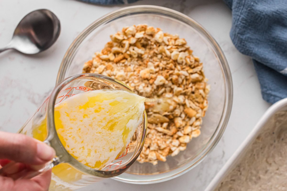 Pouring butter over crushed Ritz crackers in a mixing bowl.