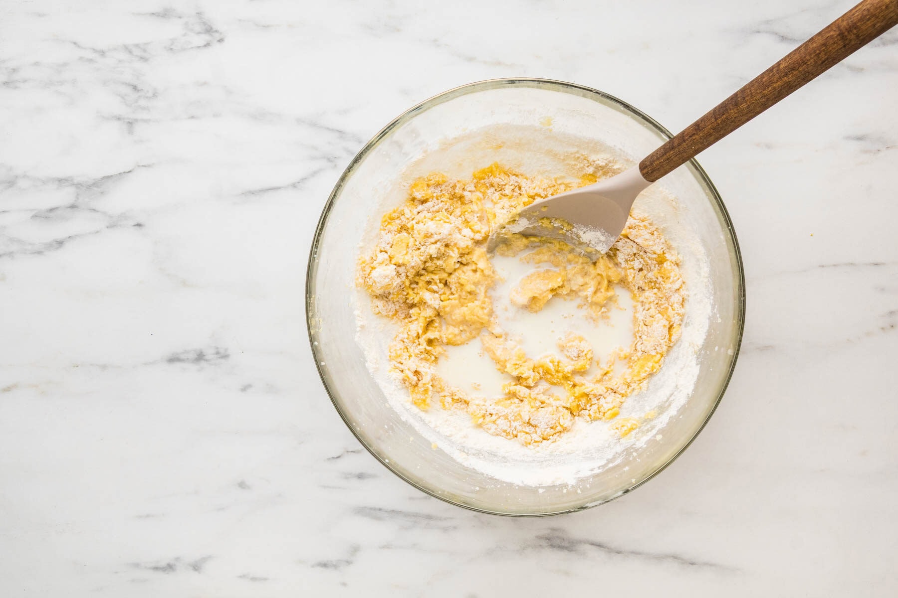 Adding milk and lemon juice to the muffin batter in a bowl.