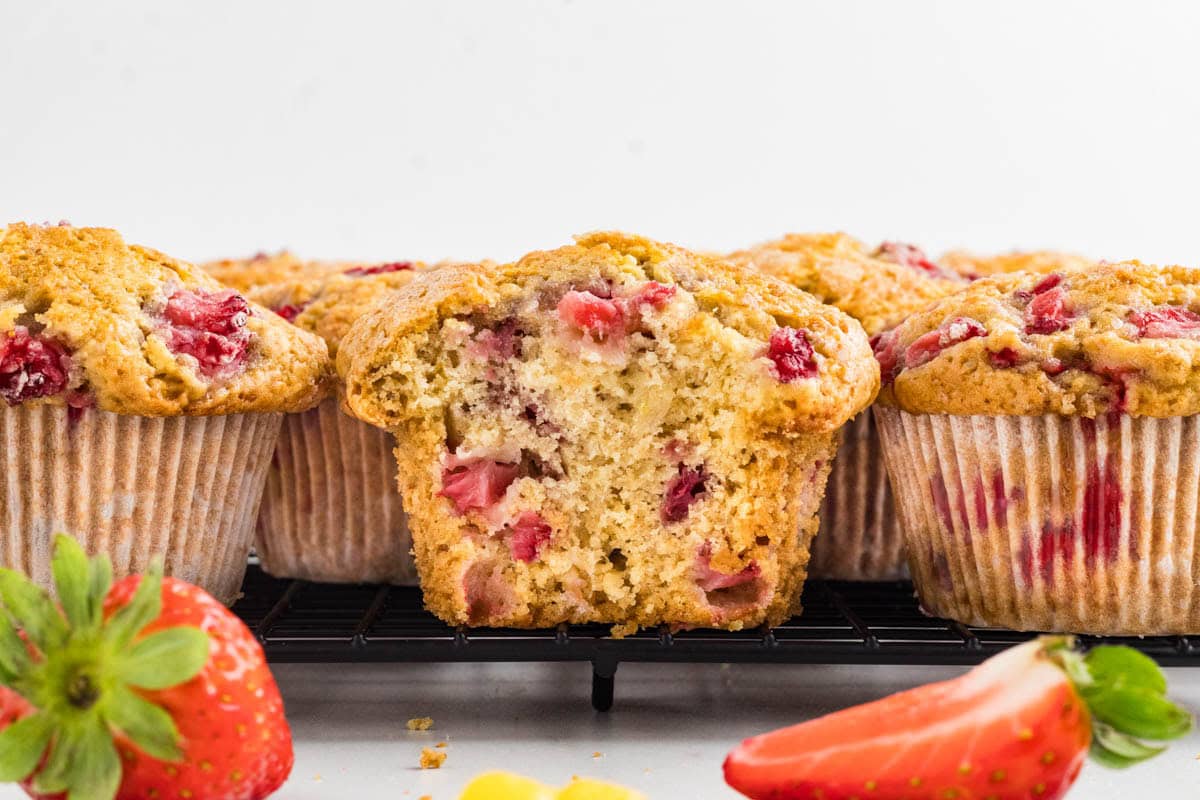 Side view of a strawberry muffin on a cooling rack with a bite missing.