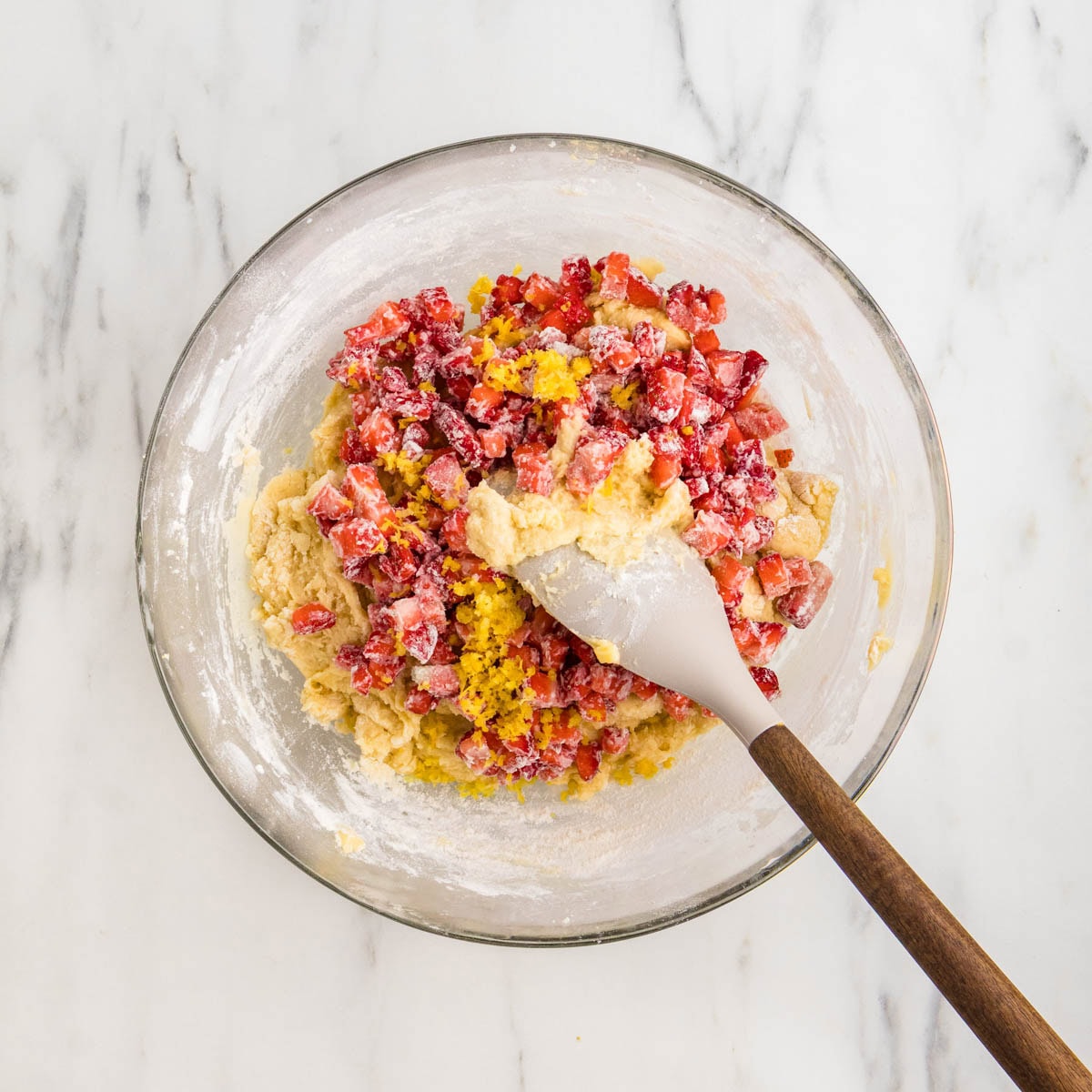 Fresh strawberries added to the muffin batter in a bowl.