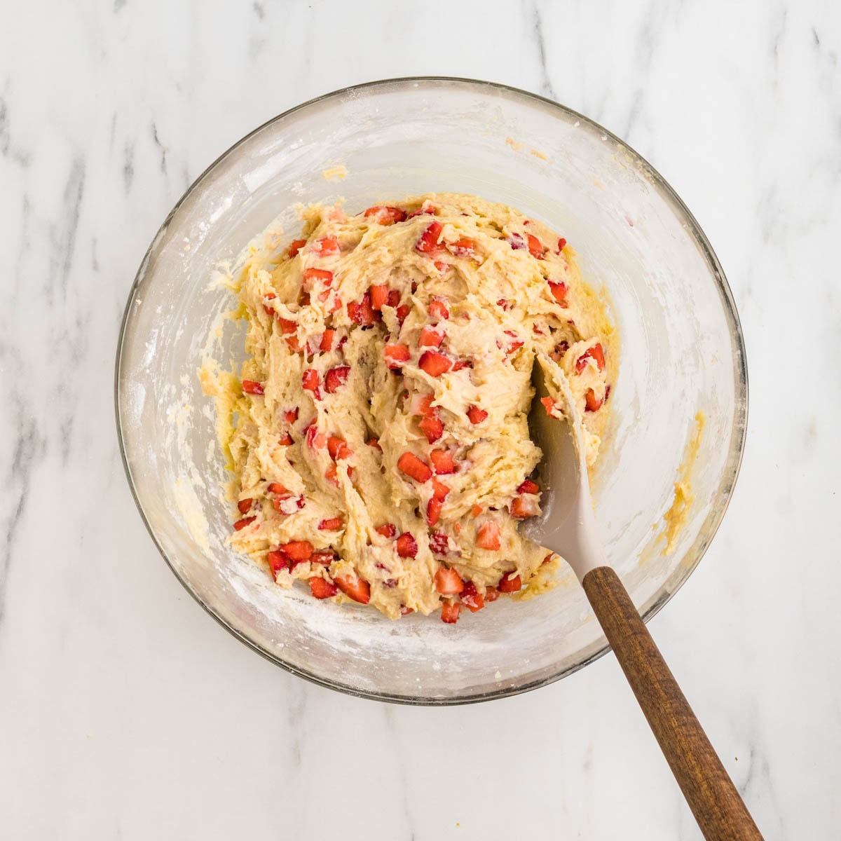 Freshly diced strawberries folded into the muffin batter in a bowl.