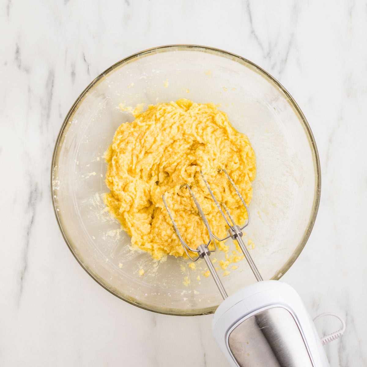 Hand mixer in a bowl after mixing the eggs and vanilla into the butter mixture.