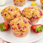 Three bakery style strawberry muffins on a plate with fresh strawberries.
