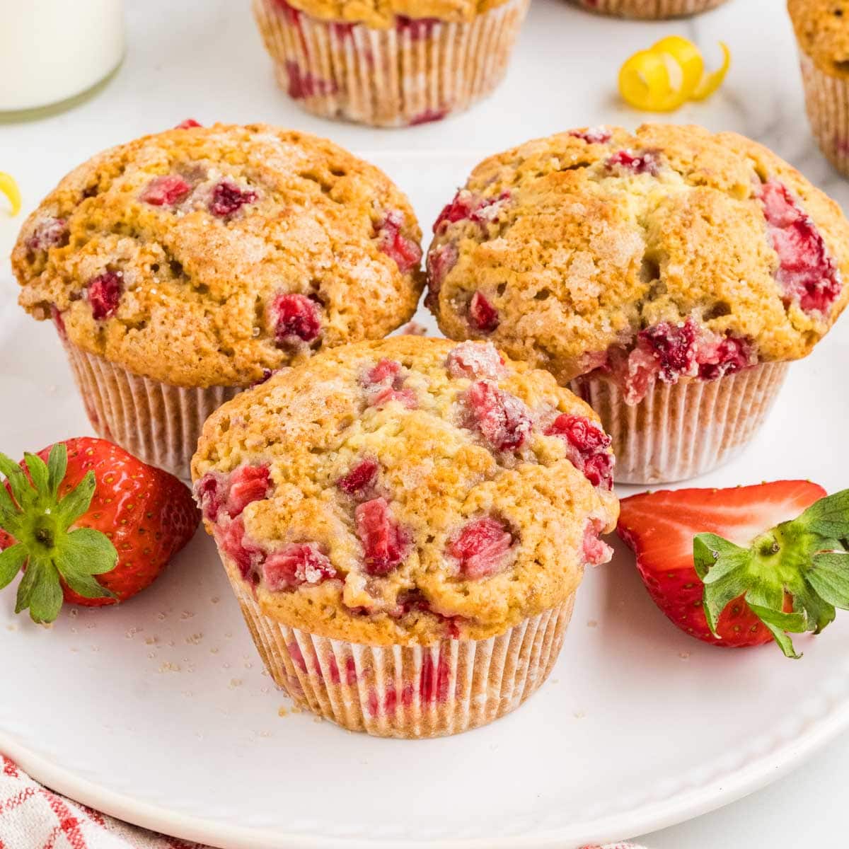 Three bakery style strawberry muffins on a plate with fresh strawberries.