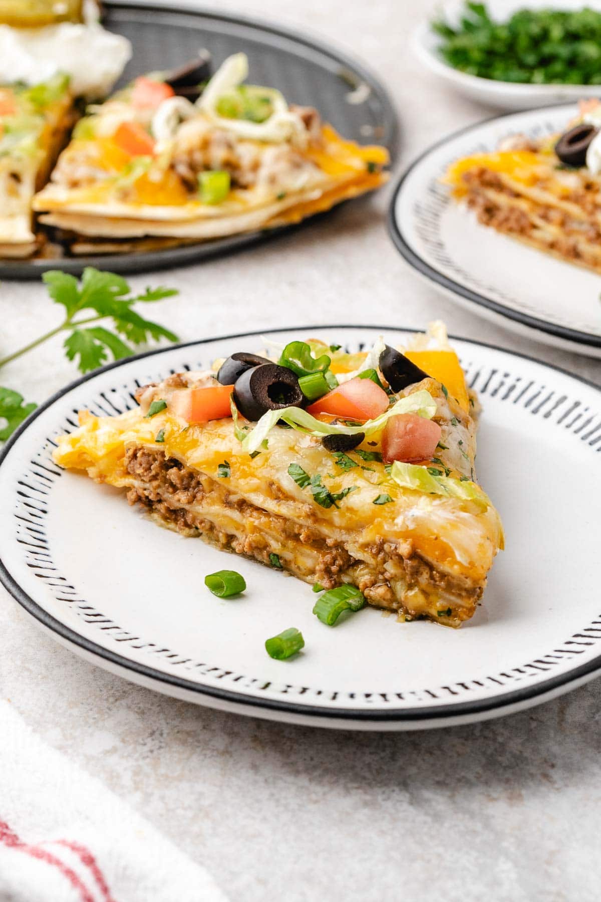 Slice of taco casserole on a plate topped with olives, tomatoes and green onions.