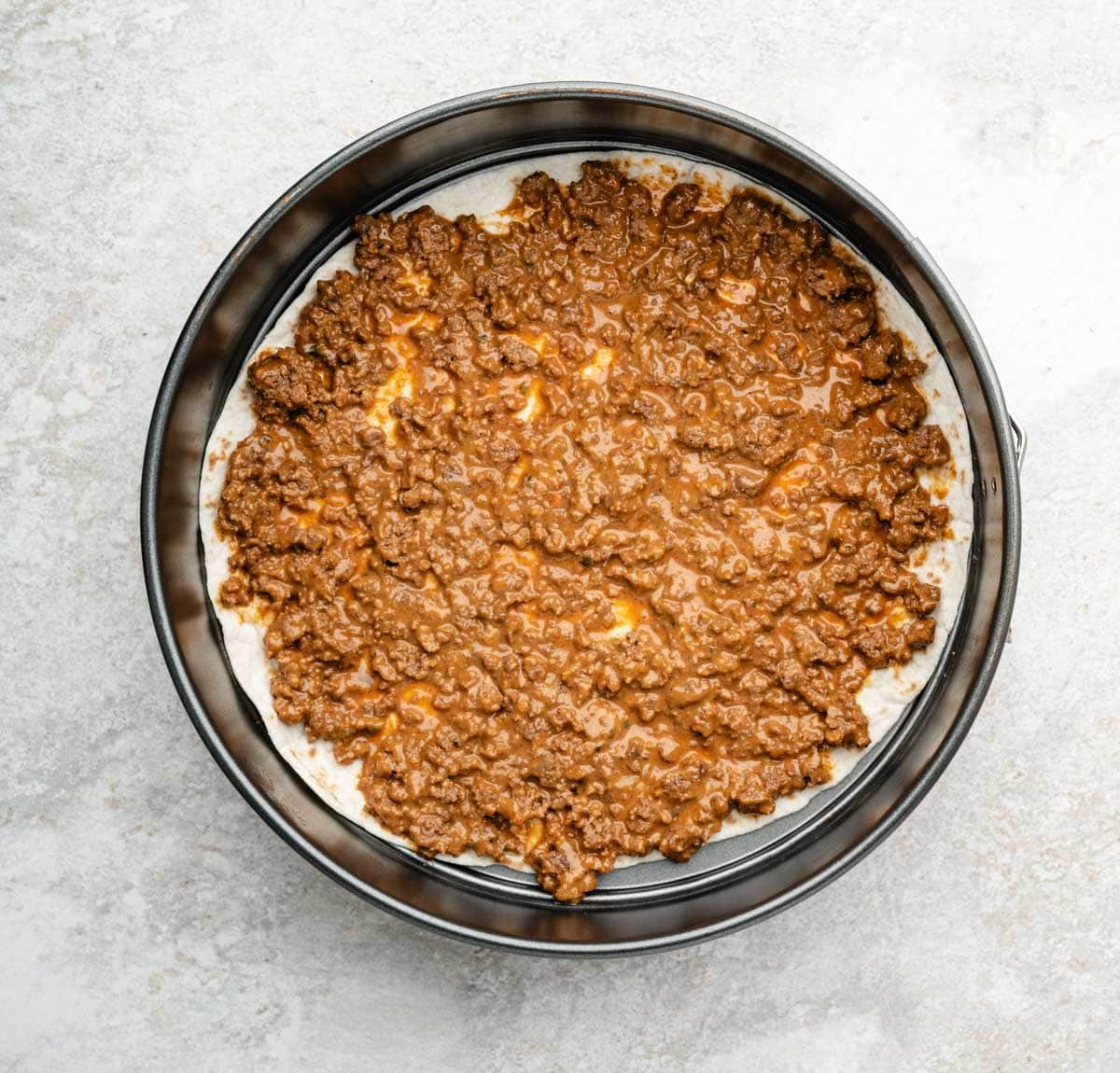 Cooked and seasoned ground beef layered on top of the tortilla in a spring form pan.