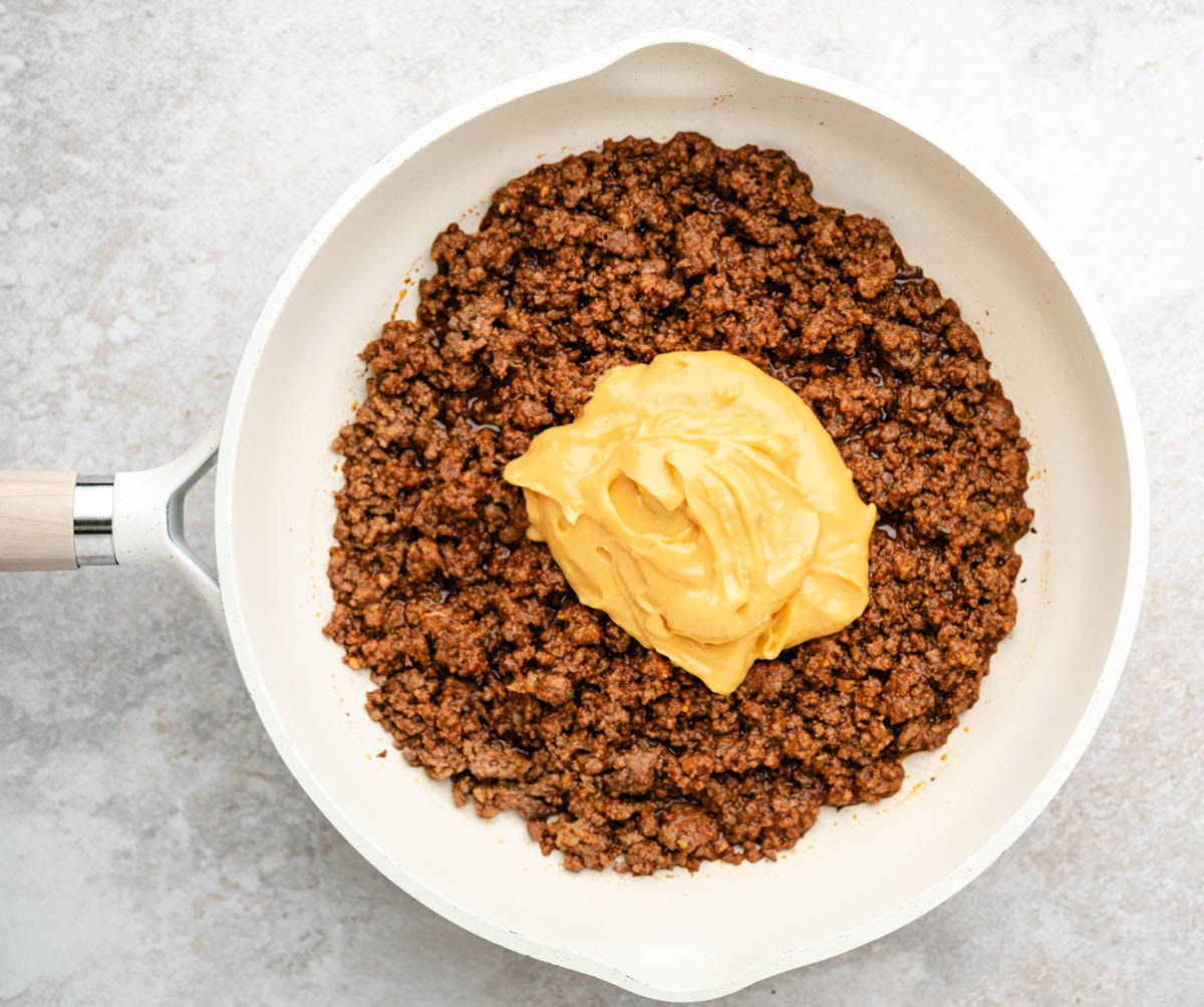 Queso cheese added to the ground beef in a skillet.