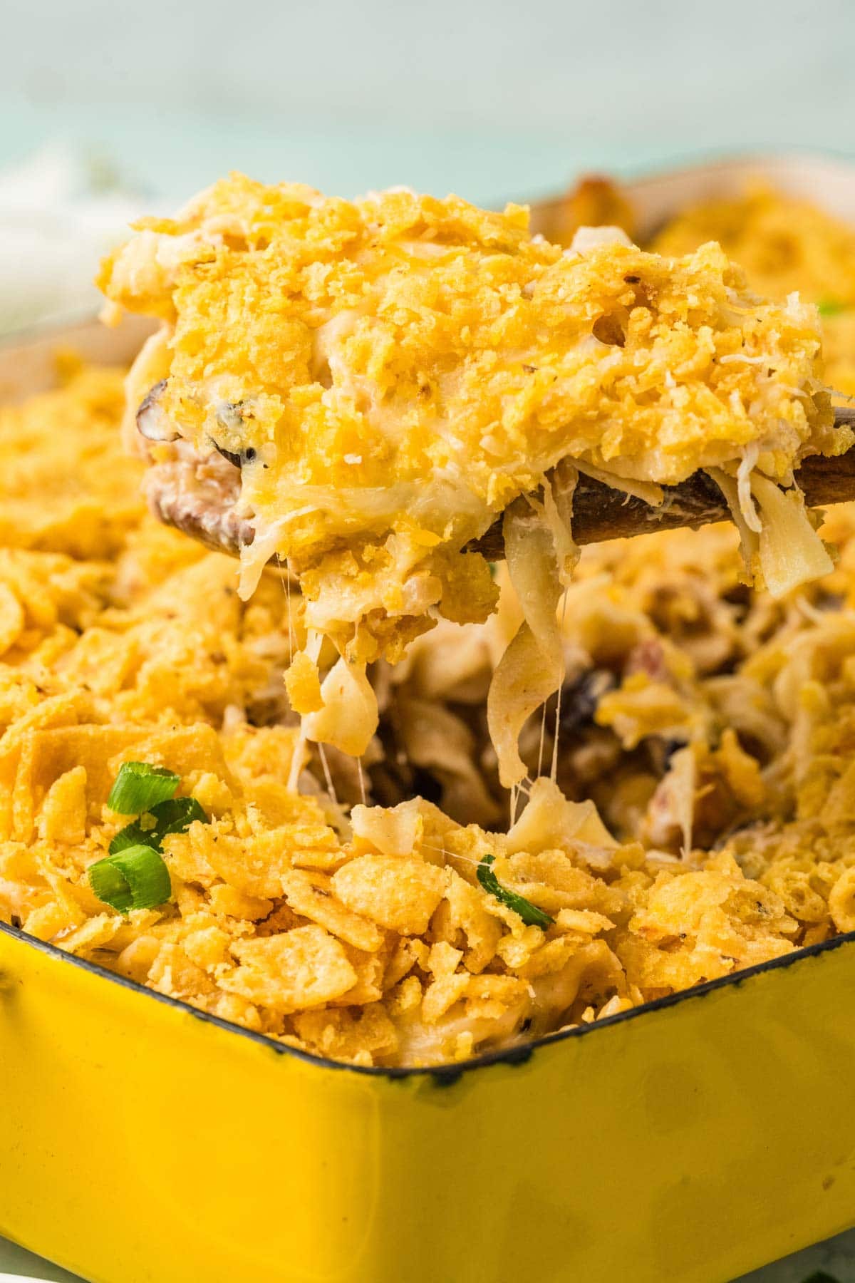 Wooden spoon taking a portion of Tex Mex chicken noodle casserole from the baking dish.