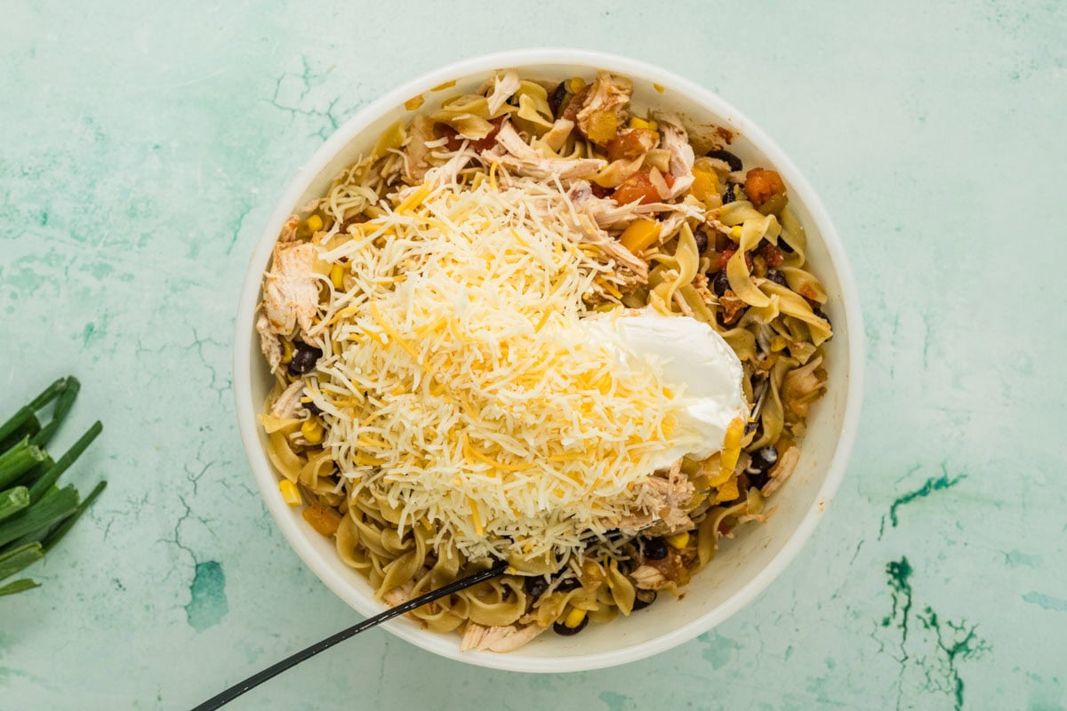 Tex mex noodle casserole mixture in a bowl with cheese and sour cream to be mixed in.