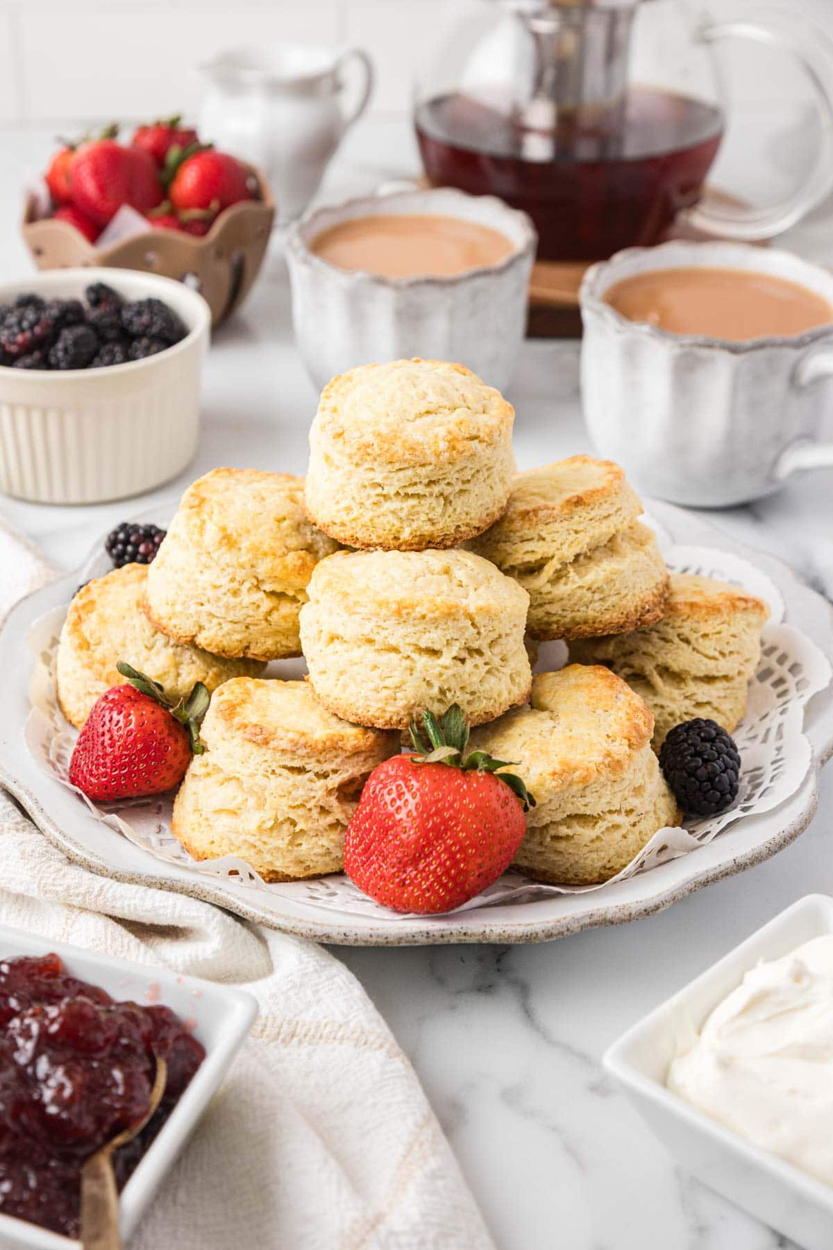 Stack of English scones served on a plate with some fresh fruit.